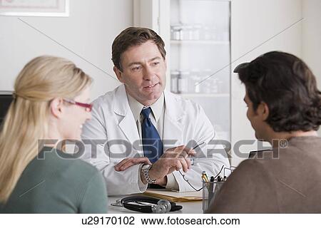 Stock Image - Male doctor talking to patients in his office. Fotosearch