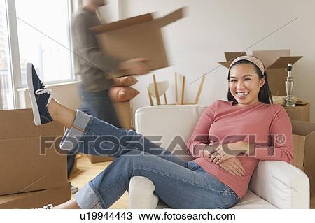 Man carrying boxes, woman resting in chair at new home View Large Photo Image Stock Image - Man carrying boxes, woman resting in chair at new home. Fotosearch