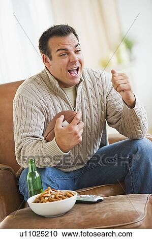 Stock Image - Man sitting on armchair watching sport on tv. Fotosearch