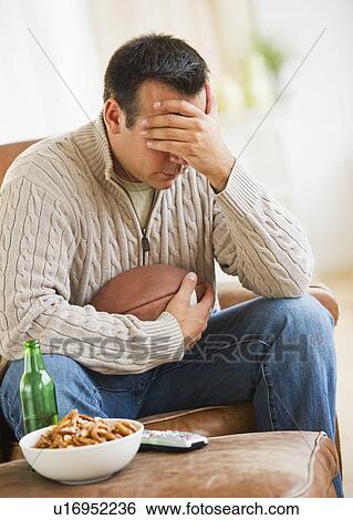 Stock Photograph - Man sitting on armchair watching sport on tv. Fotosearch