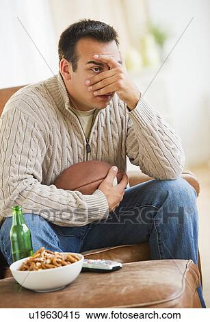 Stock Photography - Man sitting on armchair watching sport on tv. Fotosearch
