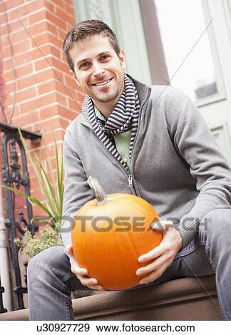 Stock Photo - Man sitting on steps with pumpkin. Fotosearch