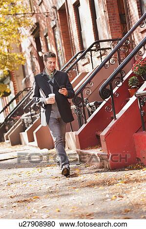 Stock Image - Man walking with mobile phone and coffee. Fotosearch