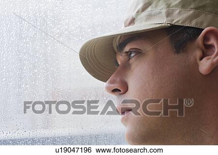 Stock Photograph - Man wearing military uniform looking through window. Fotosearch
