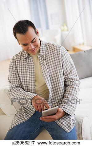 Stock Photo - Man with digital tablet sitting in living room. Fotosearch