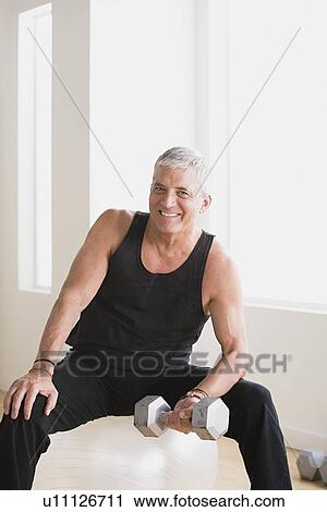 Stock Image - Mature man an lifting weights in gym. Fotosearch