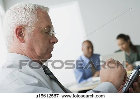 Stock Photo - Mature man texting on his mobile in office. Fotosearch