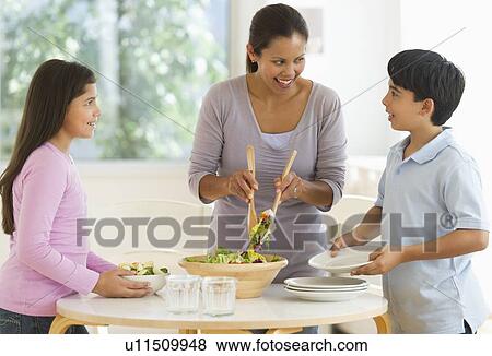 Stock Photo - Mother with son (12-13) and daughter (10-11) preparing salad. Fotosearch