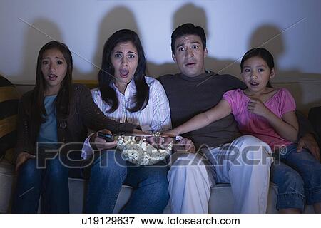 Stock Photo - Parents with two daughters (8-9, 10-11) watching tv on sofa. Fotosearch