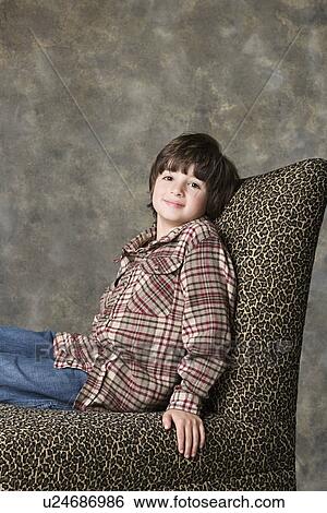 Stock Photograph - Portrait of boy (6-7) sitting on chair with animal print, studio shot. Fotosearch