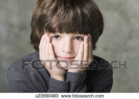 Stock Image - Portrait of boy (6-7) with face in hands, studio shot. Fotosearch