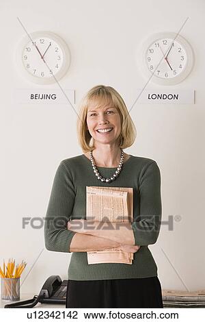 Stock Image - Portrait of businesswoman with world clocks behind. Fotosearch