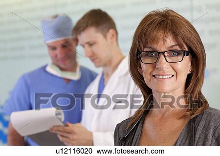Stock Image - Portrait of female doctor, male doctor and surgeon in background. Fotosearch