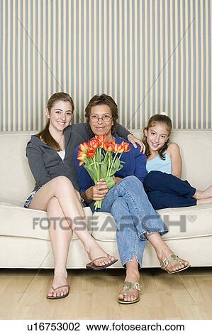 Stock Image - Portrait of grandmother and grand daughters (8-9, 14-15) sitting on sofa. Fotosearch