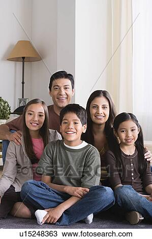 Stock Image - Portrait of happy family with three children (8-9, 10-11) sitting on floor. Fotosearch