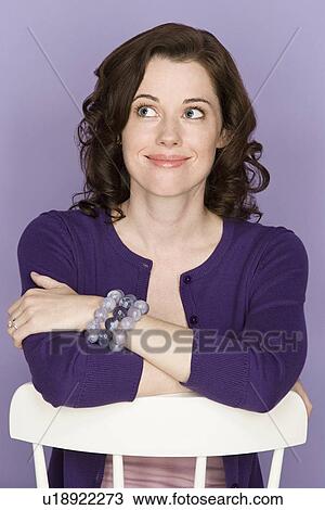 Stock Image - Portrait of happy mid adult woman leaning on white chair. Fotosearch