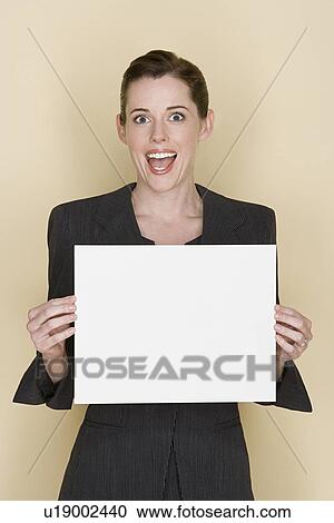 Stock Image - Portrait of happy mid adult woman holding blank sheet of paper. Fotosearch