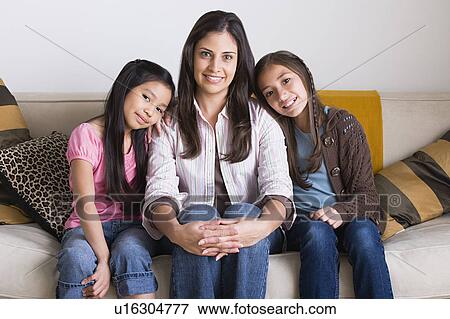 Stock Photo - Portrait of happy mother with two daughters (8-9, 10-11) sitting on sofa. Fotosearch