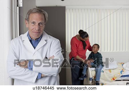 Stock Photography - Portrait of male doctor with patients in background. Fotosearch