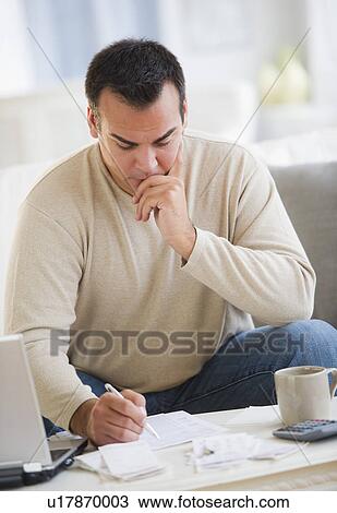 Stock Image - Portrait of man doing paperwork in living room. Fotosearch