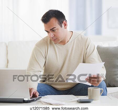 Stock Photography - Portrait of man doing paperwork in living room. Fotosearch
