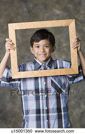 Stock Image - Portrait of smiling boy (8-9) looking through frame, studio shot. Fotosearch