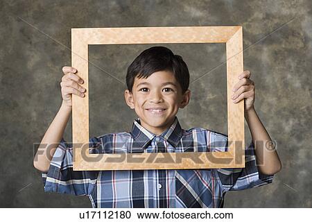 Stock Image - Portrait of smiling boy (8-9) looking through frame, studio shot. Fotosearch