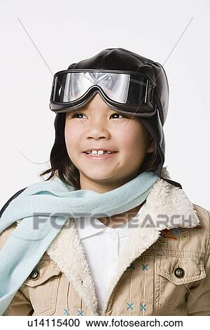 Stock Image - Portrait of smiling boy (8-9) wearing pilot hat and jacket, studio shot. Fotosearch