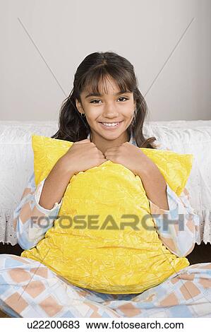 Stock Image - Portrait of smiling girl (10-11) in bed with pillow. Fotosearch