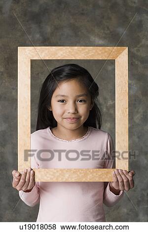 Stock Photo - Portrait of smiling girl (8-9) holding picture frame, studio shot. Fotosearch
