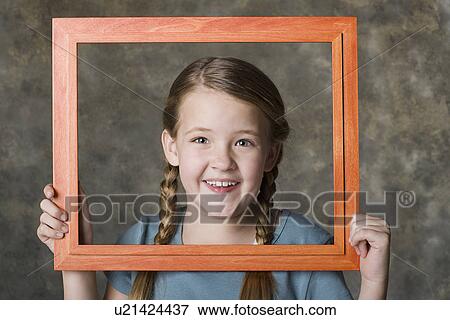 Stock Photo - Portrait of smiling girl (8-9) holding frame, studio shot. Fotosearch