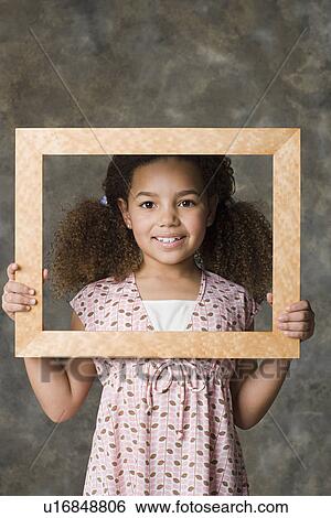 Stock Photograph - Portrait of smiling girl (8-9) holding picture frame, studio shot. Fotosearch