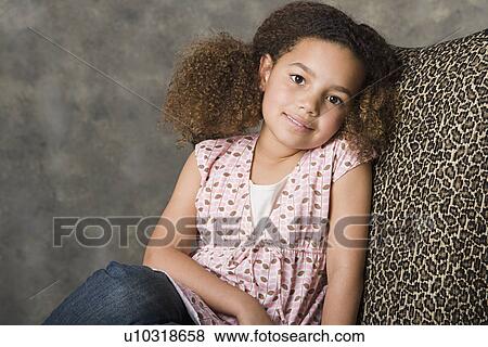 Stock Photo - Portrait of smiling girl (8-9) sitting on chair, studio shot. Fotosearch