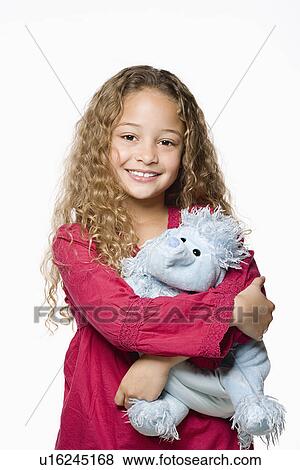 Stock Photo - Portrait of smiling girl (8-9) embracing toy, studio shot. Fotosearch