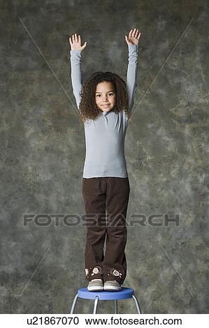 Stock Image - Portrait of smiling girl (8-9) with arms raised, studio shot. Fotosearch