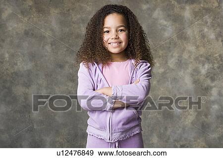 Stock Photo - Portrait of smiling girl (8-9) with arms crossed, studio shot. Fotosearch