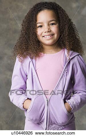 Stock Photograph - Portrait of smiling girl (8-9) with hands in pockets, studio shot. Fotosearch