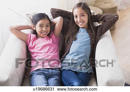 Stock Image - Portrait of smiling girls (8-9, 10-11) in armchair. Fotosearch