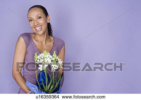 Portrait of smiling woman holding flowers on purple background, studio shot View Large Photo Image Picture - Portrait of smiling woman holding flowers on purple background, studio shot. Fotosearch
