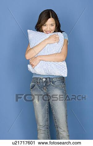 Stock Image - Portrait of smiling woman holding pillow on blue background, studio shot. Fotosearch