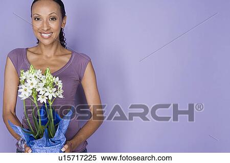 Stock Photography - Portrait of smiling woman holding flowers on purple background, studio shot. Fotosearch