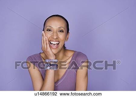 Stock Image - Portrait of smiling woman sitting on purple background, studio shot. Fotosearch