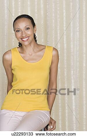 Stock Image - Portrait of smiling woman sitting on chair, studio shot. Fotosearch