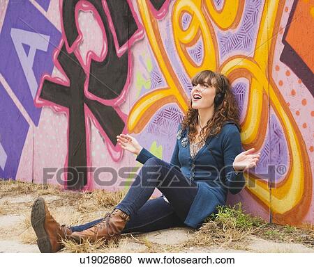 Portrait of smiling woman with headphones leaning against wall with graffiti View Large Photo Image Stock Image - Portrait of smiling woman with headphones leaning against wall with graffiti. Fotosearch