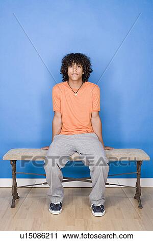 Stock Image - Portrait of teenage boy (14-15) sitting on bench. Fotosearch