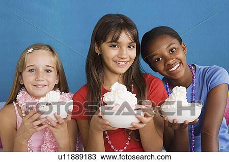 Stock Image - Portrait of three girls (10-11) holding desserts. Fotosearch