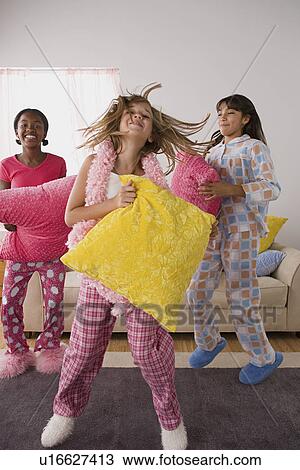 Stock Image - Portrait of three girls (10-11) jumping at slumber party. Fotosearch