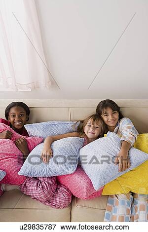 Stock Photo - Portrait of three girls (10-11) lying on sofa at slumber party. Fotosearch