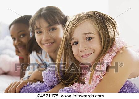 Stock Photography - Portrait of three girls (10-11) lying on bed at slumber party. Fotosearch