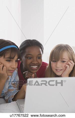 Stock Image - Portrait of three girls (10-11) using laptop. Fotosearch
